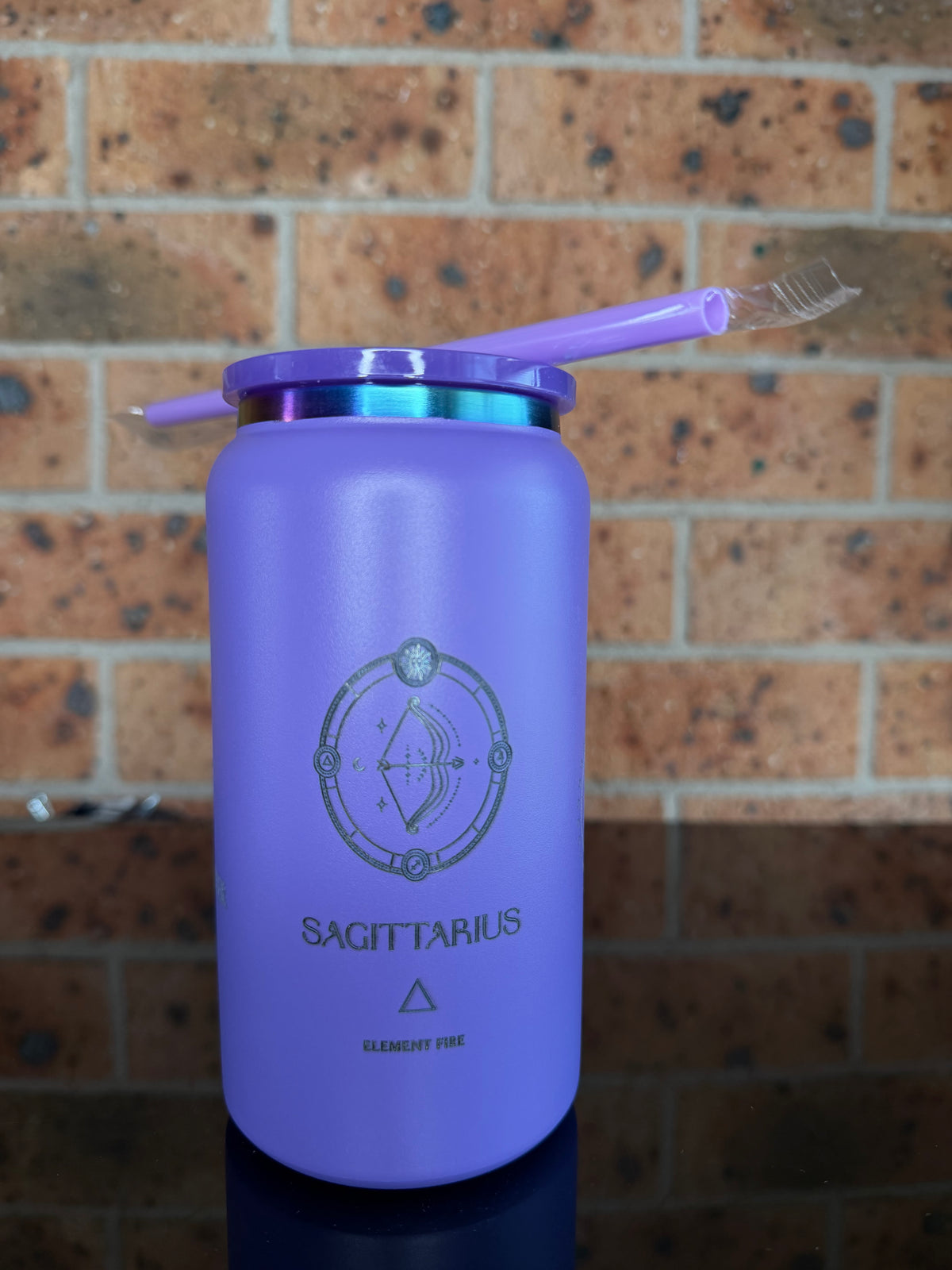 A purple insulated tumbler with a matching straw and lid, featuring a printed silver Sagittarius zodiac symbol and text, resting on a brown brick floor. Sagittarius tumbler, Sagittarius gift, engraved Sagittarius tumbler, purple travel mug, astrology gifts, zodiac stainless steel tumbler, personalized Sagittarius cup, insulated tumbler Australia.